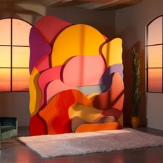 a room with two windows and a large colorful painting on the wall behind an upholstered bed