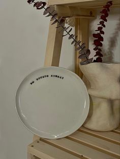 a white plate sitting on top of a wooden shelf next to a vase and plant