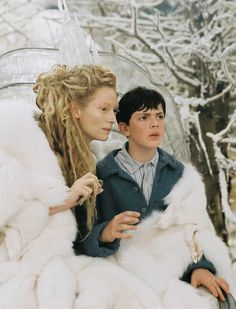 two children dressed in white furs sitting next to each other and looking at each other