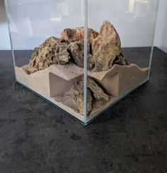 a glass box with rocks and sand inside on a black table next to a white wall