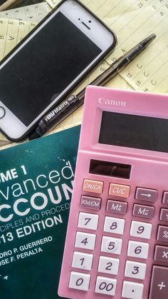 a pink calculator sitting on top of a book next to a cell phone