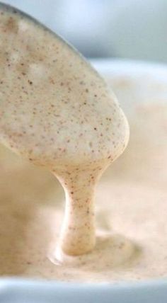 a ladle full of soup being stirred by a wooden spoon in a white bowl