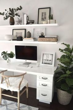 a white desk topped with a computer monitor next to a plant and potted plants