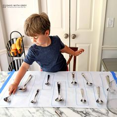 a young boy sitting at a table with silverware on it