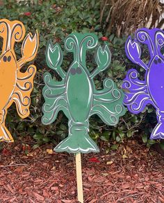 three wooden cutouts of different shapes and sizes sitting on top of the ground in front of some bushes