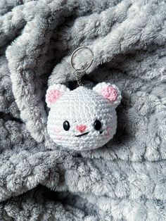 a crocheted kitty keychain is laying on a gray blanket with pink ears