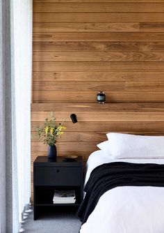 a bedroom with wood paneling and white bedding, black night stand and nightstand