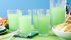 two glasses filled with green liquid next to bowls of food