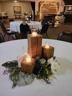 candles are placed on top of wooden blocks in the center of a table with flowers and greenery