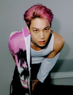 a young man with pink hair is leaning against a wall