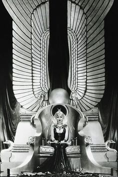 an old photo of a woman sitting on a chair in front of two large wings