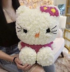 a woman sitting on the floor holding a hello kitty stuffed animal with roses all over it