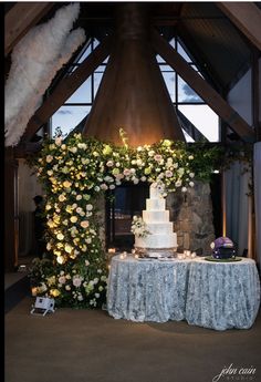 a white wedding cake sitting on top of a table next to a flower covered arch