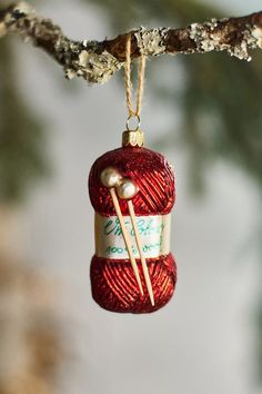 a red yarn ornament hanging from a tree branch with knitting needles in it