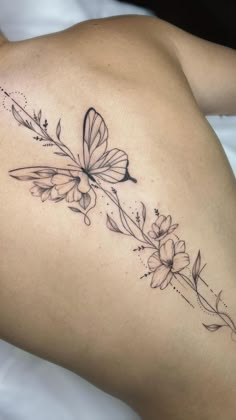 a woman's back with a butterfly and flowers tattoo on her left side ribcage