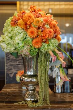 a silver vase filled with lots of flowers on top of a wooden table next to a mirror