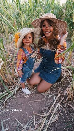 two women in overalls and hats are sitting in the middle of a corn field