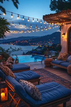 an outdoor living area with blue couches and lights strung over the pool at night