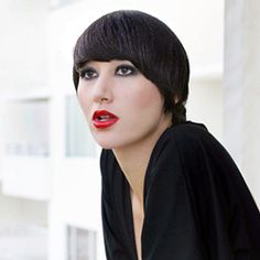 a woman with short black hair and red lipstick posing for a photo in front of a building