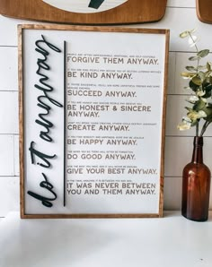 a wooden sign sitting on top of a white counter next to a vase with flowers