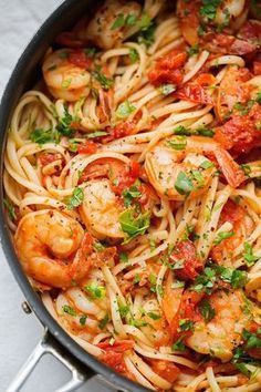 pasta with shrimp, tomato sauce and parsley in a skillet on a white surface