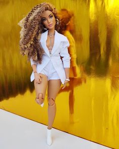 a barbie doll is standing in front of a yellow wall