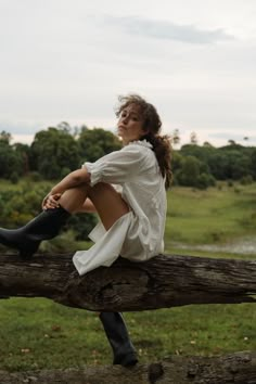 a woman sitting on top of a tree branch with her legs crossed and wearing rain boots