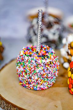 an apple covered in sprinkles sitting on top of a wooden table next to other desserts