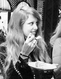 a woman eating food from a plate in front of another woman sitting at a table