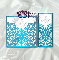 two blue snowflakes cut out of paper on a white satin background with the words boody's designs