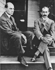 black and white photograph of two men sitting on the front steps of a house, one wearing a suit