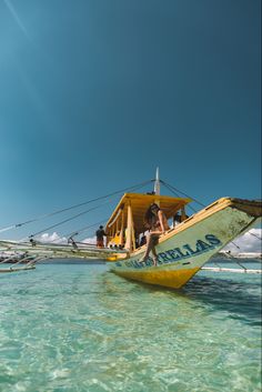 people are riding on the back of a yellow boat in clear blue water with other boats behind them