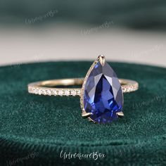 a tan gold engagement ring with a blue sapphire and diamond accents on the band, sitting on a green velvet box