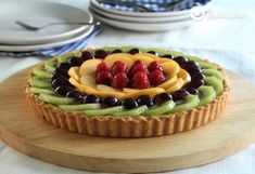 a fruit tart on a wooden platter with plates in the background