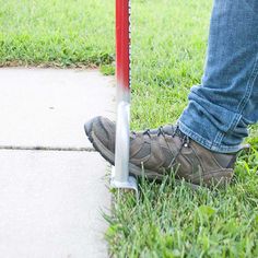 a person standing next to a red and white pole on the grass near a sidewalk