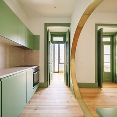 an empty kitchen with green cabinets and wood flooring is seen through a circular mirror