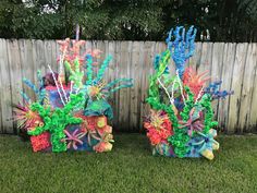 two vases made out of plastic are sitting on the grass in front of a fence