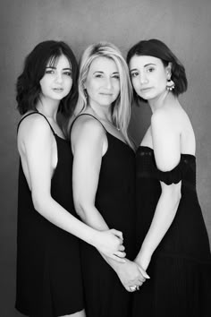 three women in black dresses are posing for a photo with their arms around each other