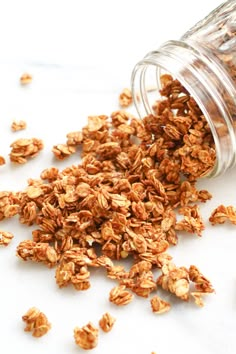 an open jar filled with granola on top of a white counter next to a pile of nuts