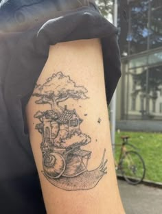 a man's arm with a snail and house tattoo on the back of his arm