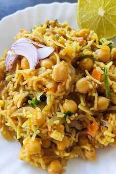 a white plate topped with rice and beans next to a lemon wedge on top of a table