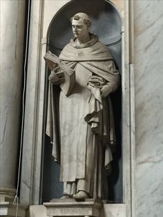 a statue of a man holding a book in his hands and standing next to a wall