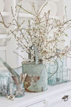 an old watering can filled with flowers on top of a white dresser in a kitchen