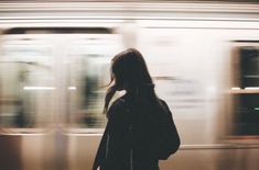 a woman standing in front of a train at a subway station with the lights on