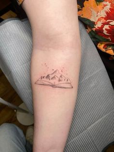 a small tattoo on the arm of a person with a book in front of them