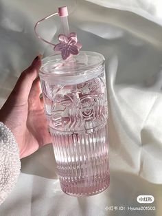 a hand holding a pink glass cup with a flower on it and a string attached to the top