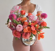 a woman holding a disco ball filled with lots of pink and orange flowers in her hands