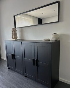 a large black cabinet with two vases on top and a mirror above it in a room