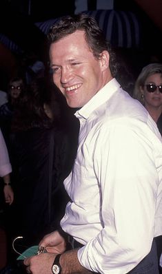 a man in a white shirt and tie smiles at the camera while standing next to other people