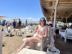 a woman sitting in a chair on the beach eating an ice cream sunbather